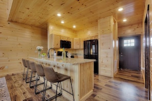 Ein Holzblockhaus-Interieur mit Kücheninsel, Barhocker und Kühlschrank.