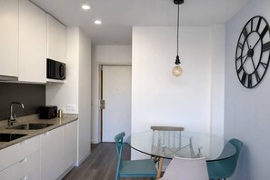 A modern kitchen with white cabinets, a microwave, and a sink. There is a glass dining table with chairs and a pendant light. - Downtown Porto. Trindade Metro. (Porto)