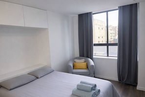A hotel room with a bed, a chair, a window with curtains, and a view of buildings outside. - Downtown Porto. Trindade Metro. (Porto)