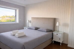 Quarto com uma cama grande, duas mesas de cabeceira com luminárias, uma janela com vista e cama bem arrumada com toalhas.