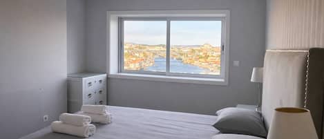 Une chambre d’hôtel dotée d’une grande fenêtre, d’un lit, d’une table de chevet avec des lampes et offrant une vue sur le paysage urbain.
