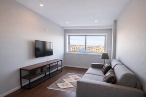A modern living room with a flat-screen TV, a sofa, a coffee table, and a window with a city view. - Panoramic Douro View | Bridge & City Centre (Vila Nova de Gaia)