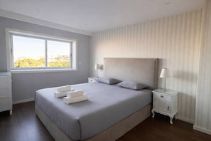 A bedroom with a large bed, two bedside tables, a window, and a view of greenery outside. - Panoramic Douro View | Bridge & City Centre (Vila Nova de Gaia)