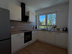 Una cuina moderna amb armaris blancs, forn integrat i una finestra que deixa entrar llum natural.