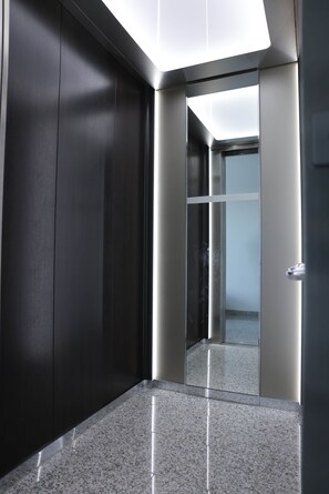 A modern elevator with a glass door, a polished granite floor, and a dark wall.