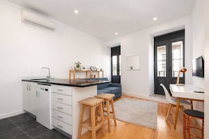 A modern kitchen with a built-in dishwasher, a dining area with a white table and chairs, and a blue sofa. - Downtown Riverside Gaia, Porto (Vila Nova de Gaia)