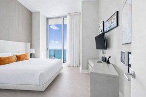 Habitació d'hotel amb un llit gran, una taula de treball i una televisió de pantalla plana, i vista a l'oceà a través d'una porta corredissa de vidre.
