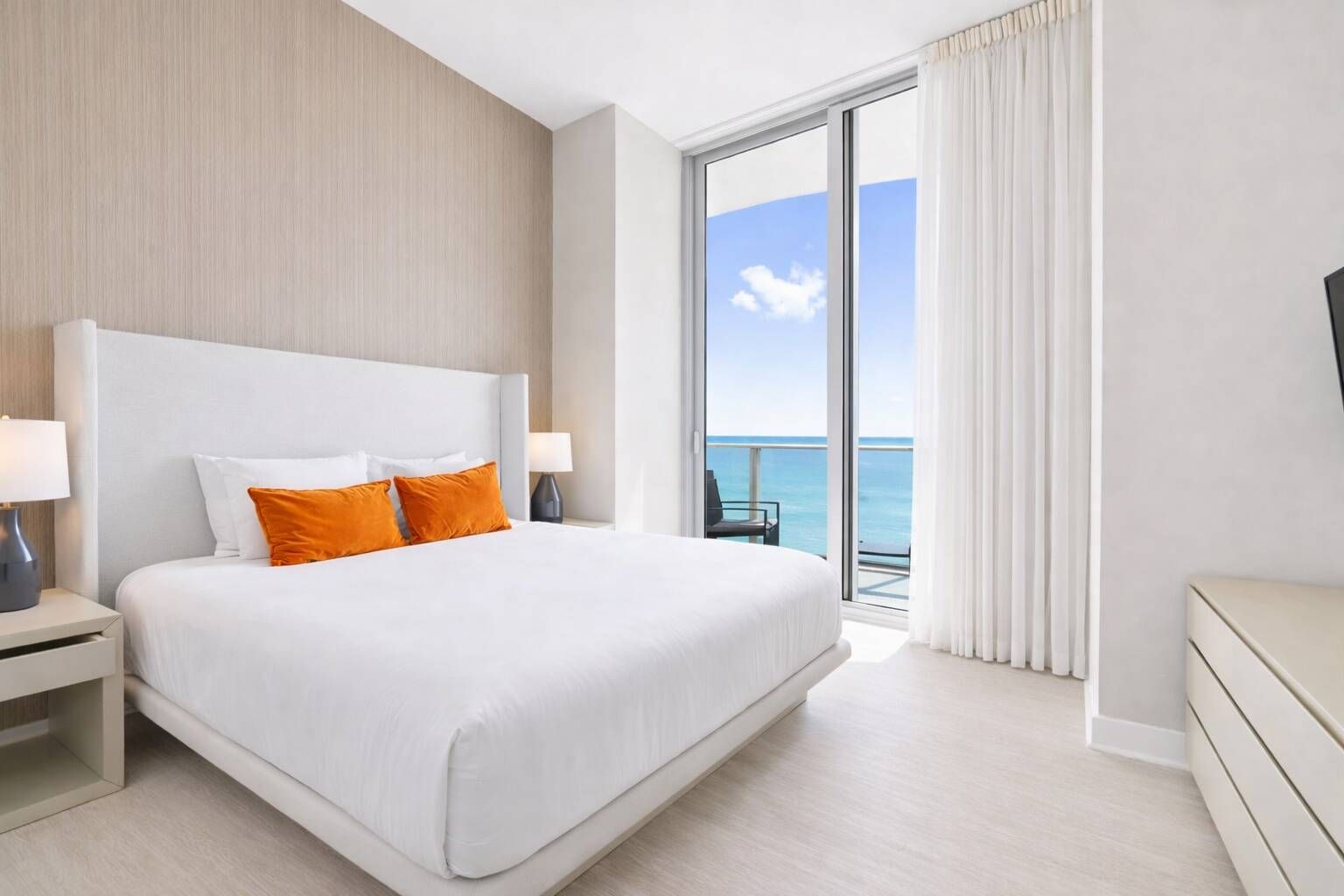 A hotel room with a large bed, a nightstand, a TV, and a view of the ocean.