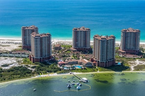 A high-rise hotel with multiple floors, a beach view, and a marina with boats. - Portofino Island Resort 2-1101 (Pensacola Beach)