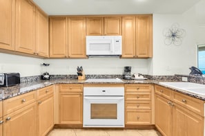 A kitchen with wooden cabinets, a microwave, a toaster, a coffee maker, and a stove. - Portofino Island Resort 2-1101 (Pensacola Beach)