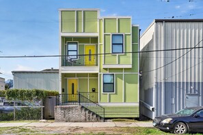 A multi-story residential building with a green facade, a yellow door, and a staircase leading to the entrance. - Renovated Home 3BA Near French Quarter & Superdome (New Orleans)