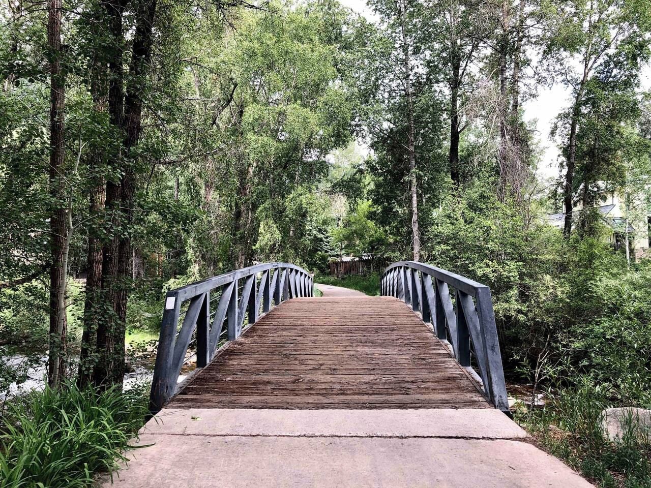 A wooden bridge with metal railings in a forested area.