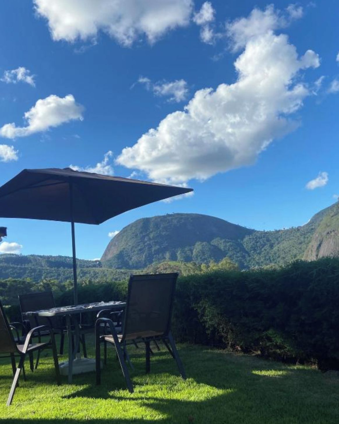 An outdoor seating area with a table and chairs, a large umbrella, and a view of a mountainous landscape.