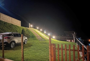 A gated area with a vehicle parked on a grassy slope, a wooden fence, and a building in the background. - Casa Refúgio  (Teresópolis)