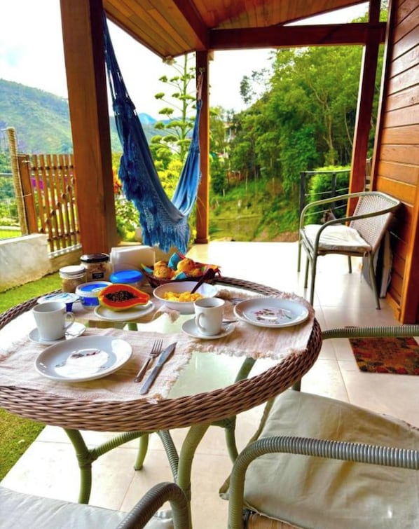 A covered outdoor dining area with a wicker table, chairs, and a hammock.