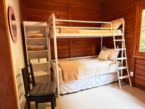 A bunk bed with a ladder, a chair, and a shelf unit in a room with wooden walls.