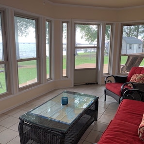 A sunlit room with large windows, a glass-top table, wicker furniture, and a view of a body of water and a dock. - Waterfront Spacious 4-bedroom house on Toledo Bend in Hemphill (Hemphill)