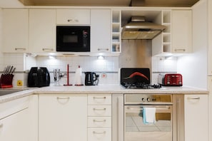 A kitchen with white cabinets, a microwave, a toaster, a kettle, and a stove. - Studio Flat with Waterfront Views in East London (Greater London)