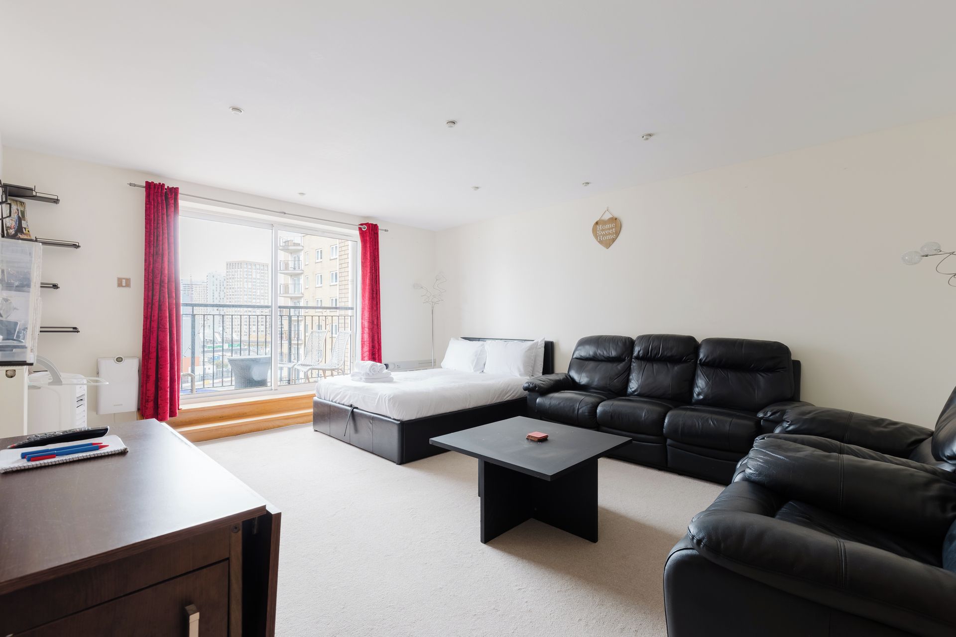 A modern living room with a sofa, a bed, a desk, and a window with curtains.
