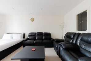 A modern hotel room with a black leather sofa, a black coffee table, and a bed with white bedding. - Studio Flat with Waterfront Views in East London (Greater London)