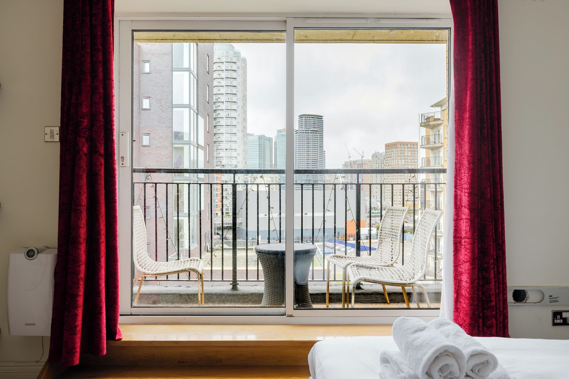 Habitación de hotel con balcón, una cama con toallas dobladas y vistas a edificios de la ciudad.