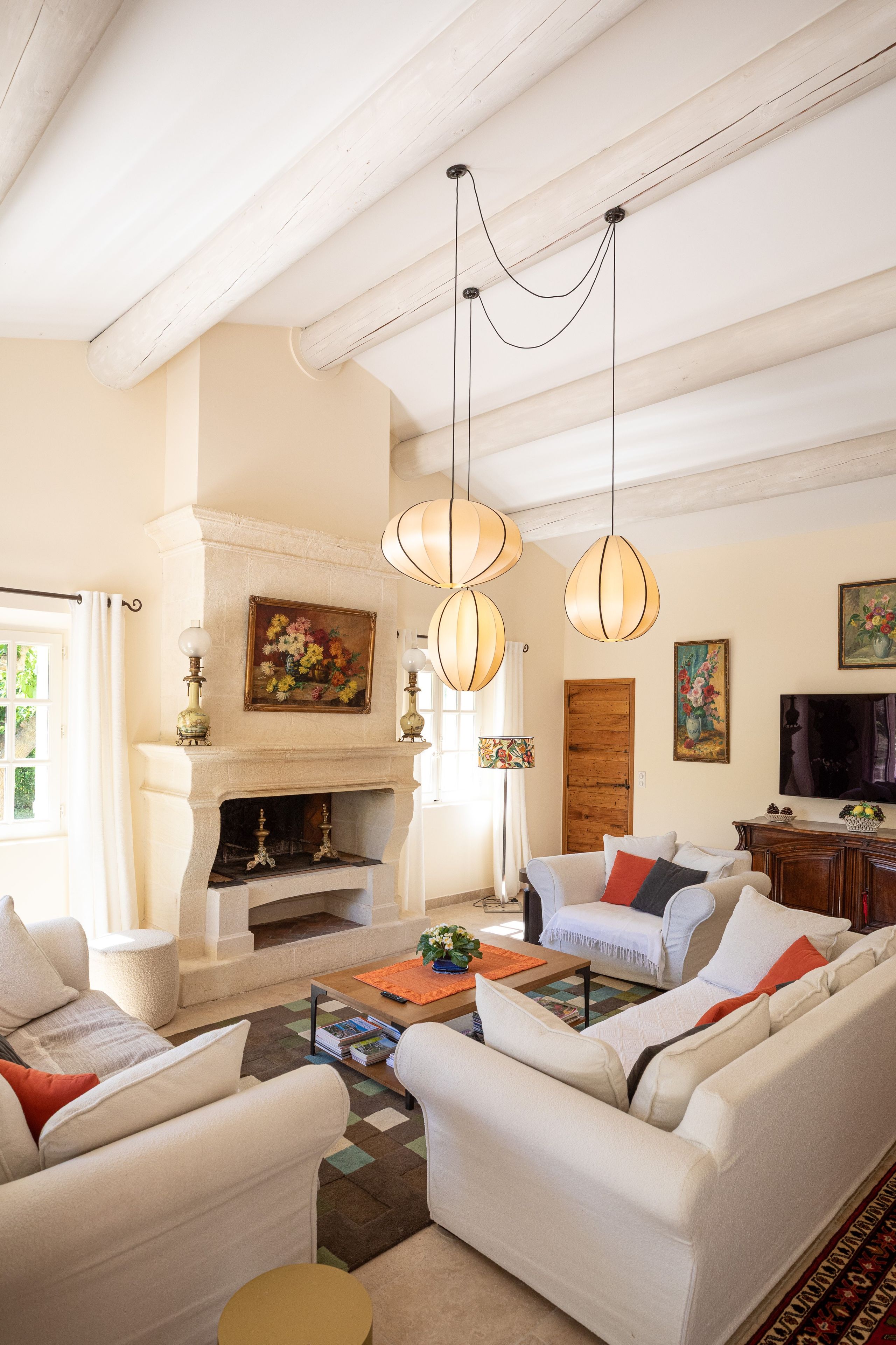 Un salon bien éclairé, doté d’une cheminée, de canapés blancs et de lampes suspendues.