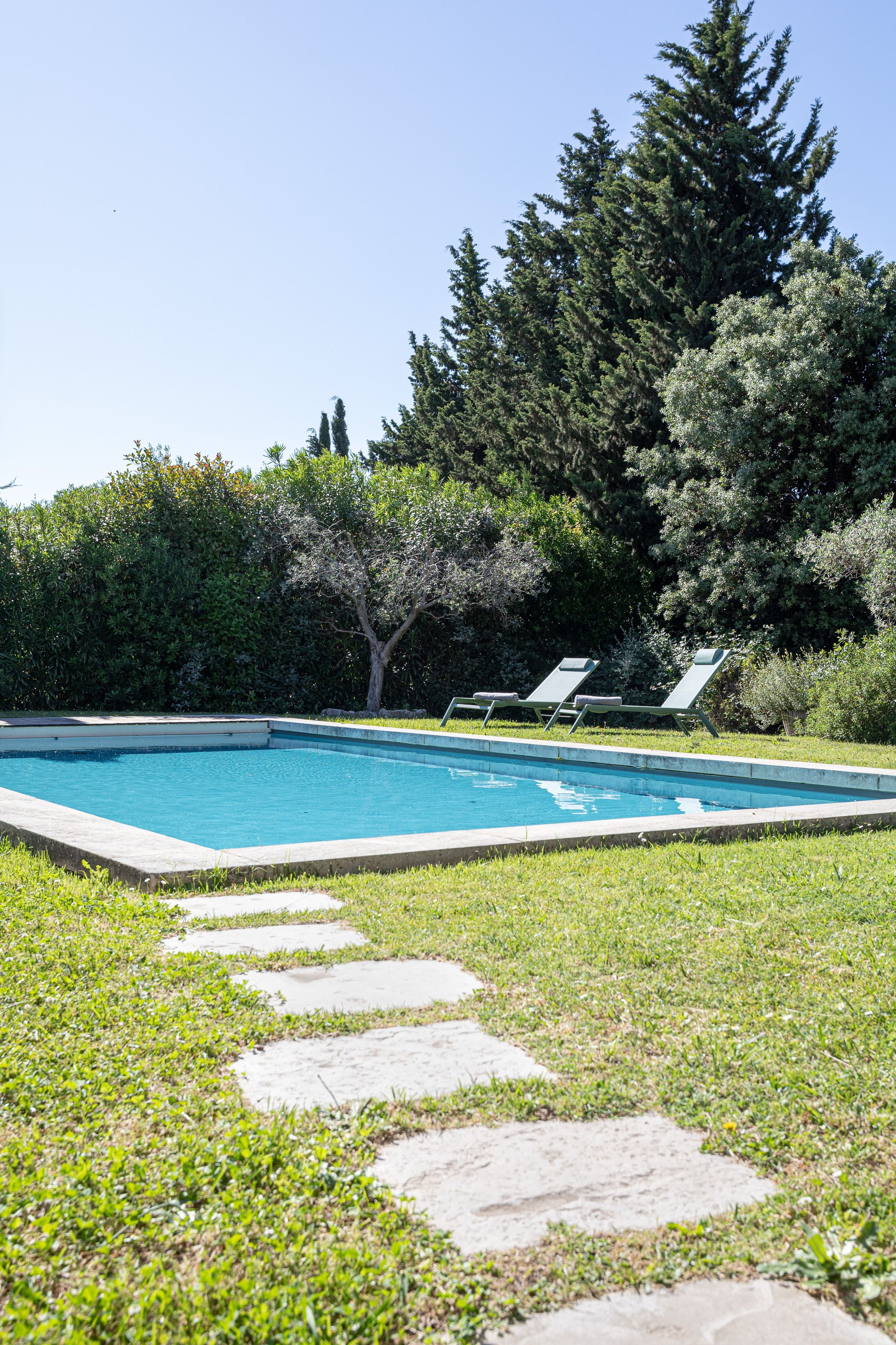 Une piscine avec un chemin de pierre menant à des chaises longues.