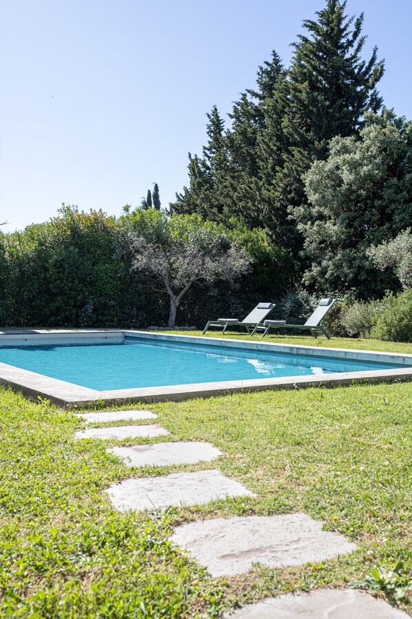 Une piscine avec un chemin de pierre menant à des chaises longues.
