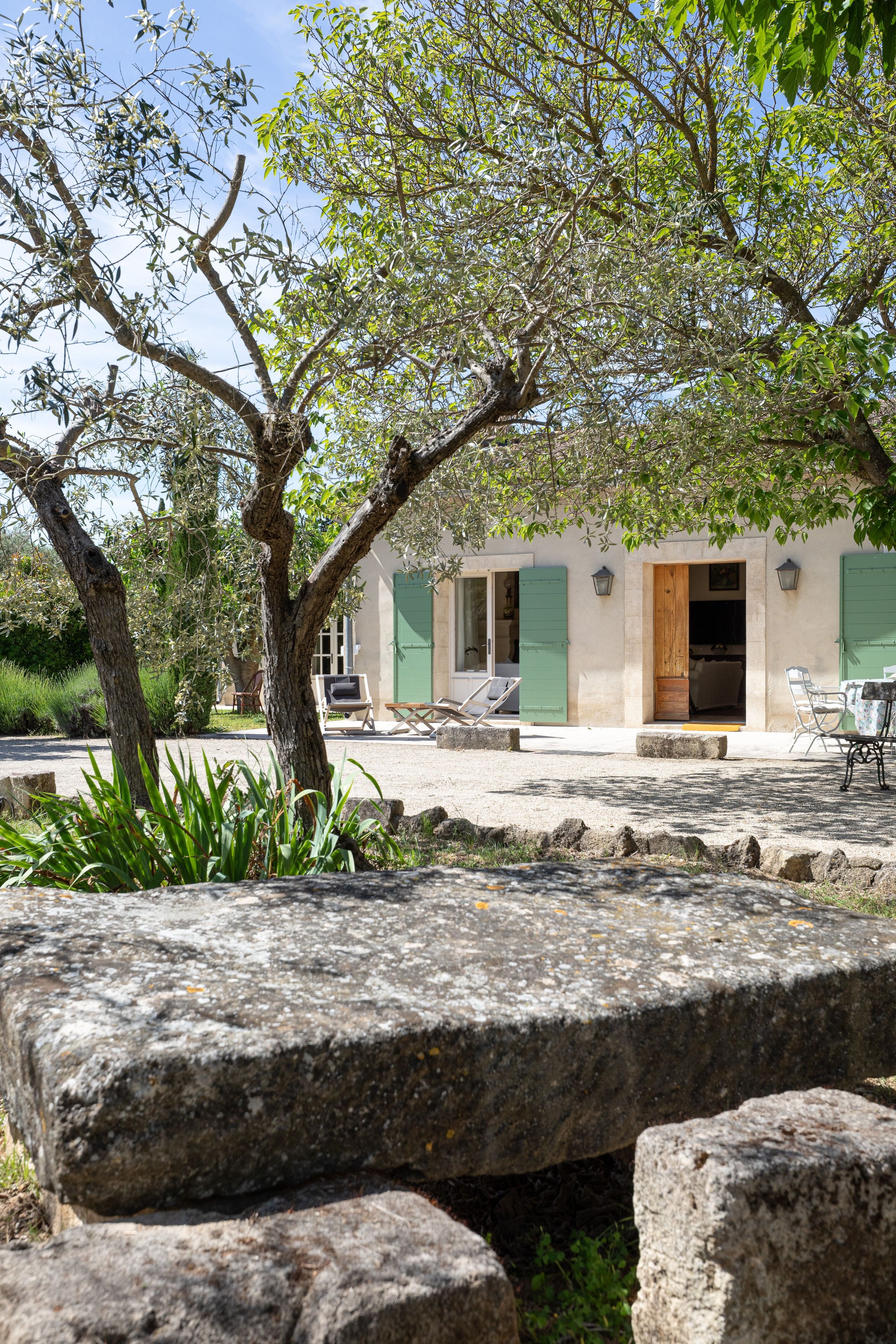 A rustic building with a stone facade, a wooden door, and a green shutter. There are outdoor seating areas with chairs and tables.