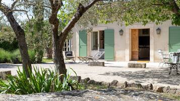 A rustic building with a stone facade, a wooden door, and a green shutter. There are outdoor seating areas with chairs and tables.