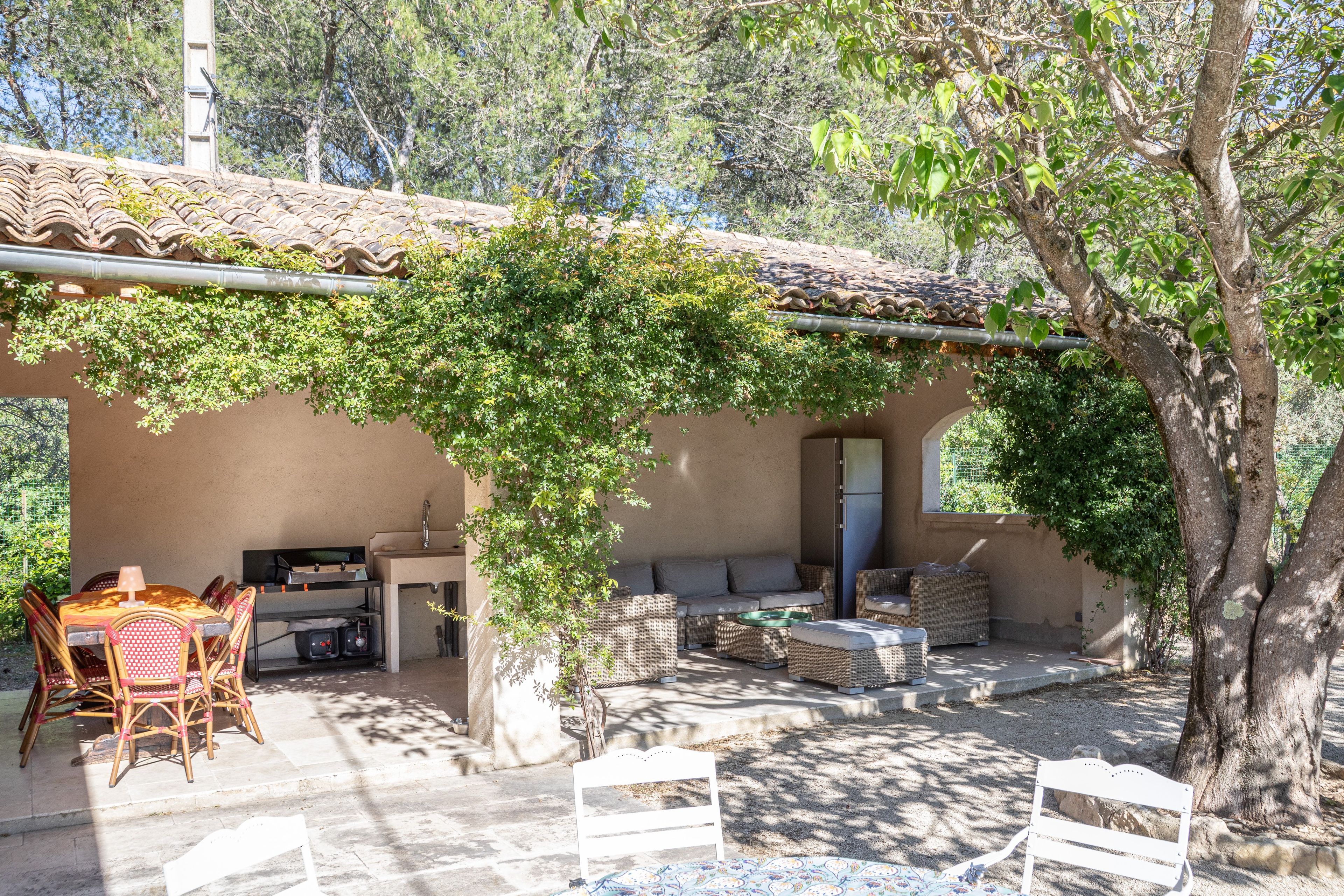 An outdoor patio with a table and chairs, a sofa, and a pergola covered in greenery.