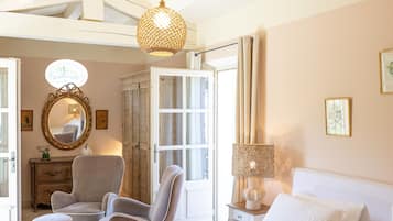 A bedroom with a bed, two chairs, a dresser, a mirror, a hanging light fixture, and a window.