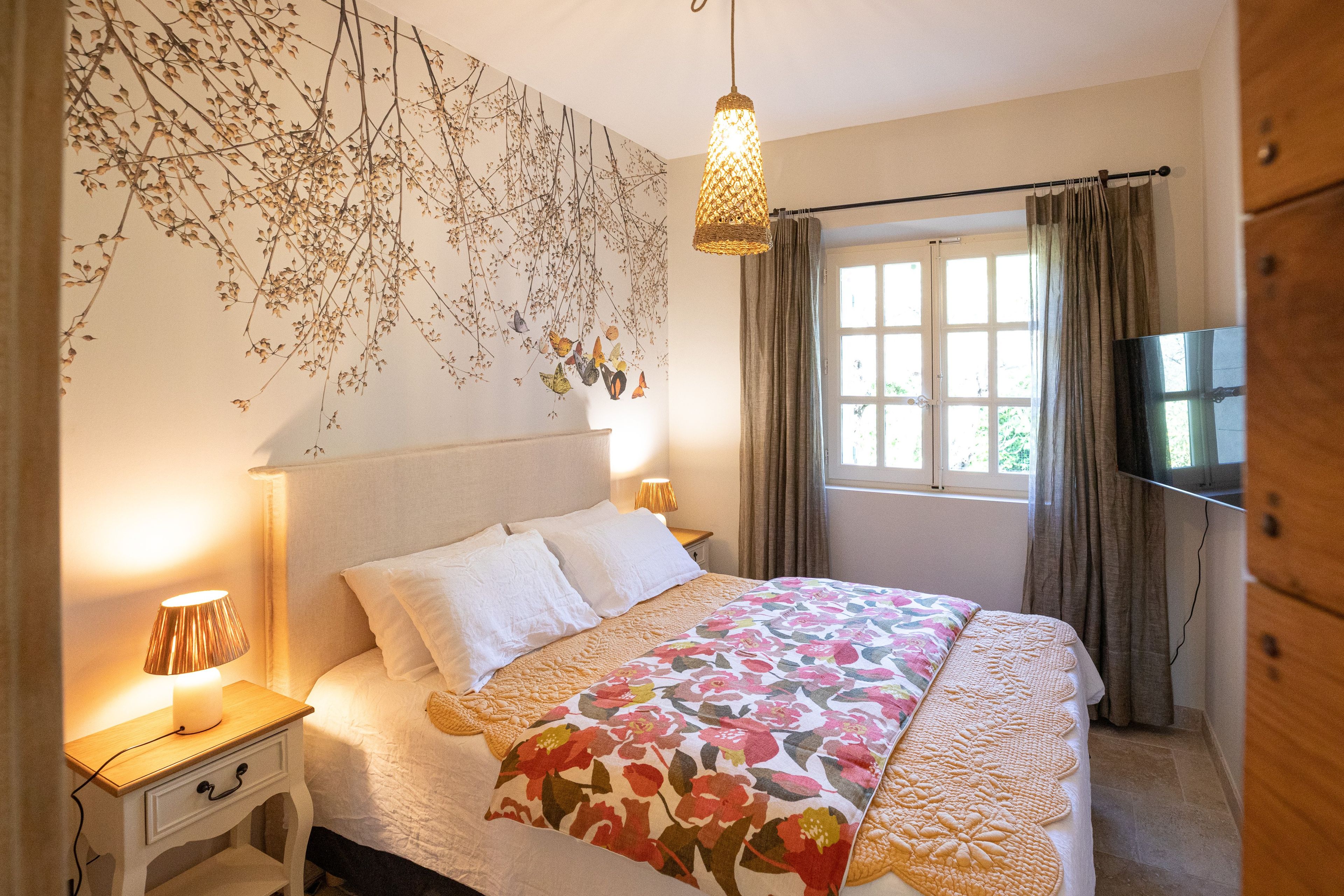 Une chambre à coucher avec un lit, des lampes de chevet, une fenêtre avec des rideaux et un élément décoratif mural.