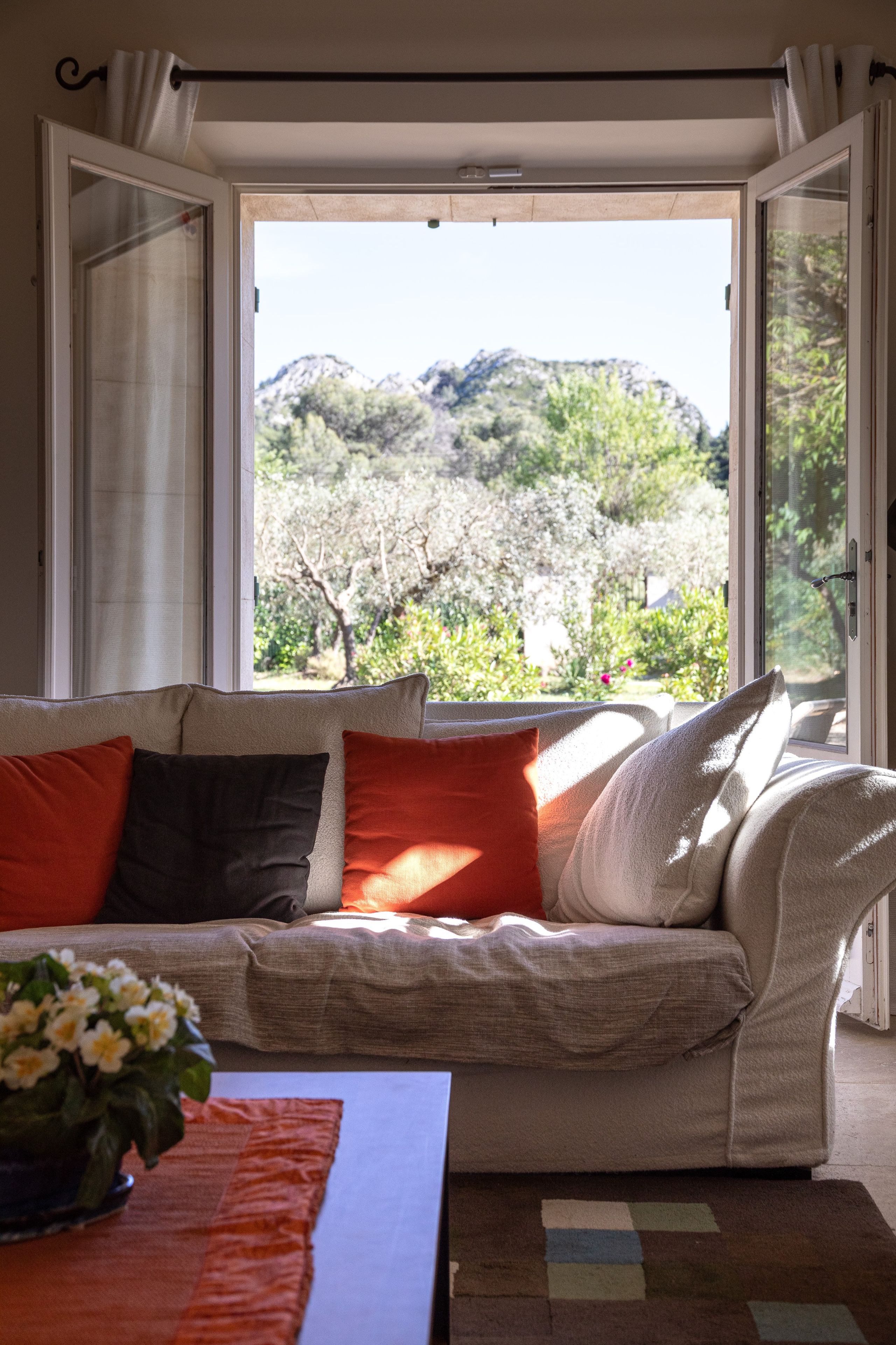 Une pièce avec un canapé placé face à une grande fenêtre, d’où l’on peut admirer un paysage montagneux, et une petite table sur laquelle est posé un vase de fleurs.