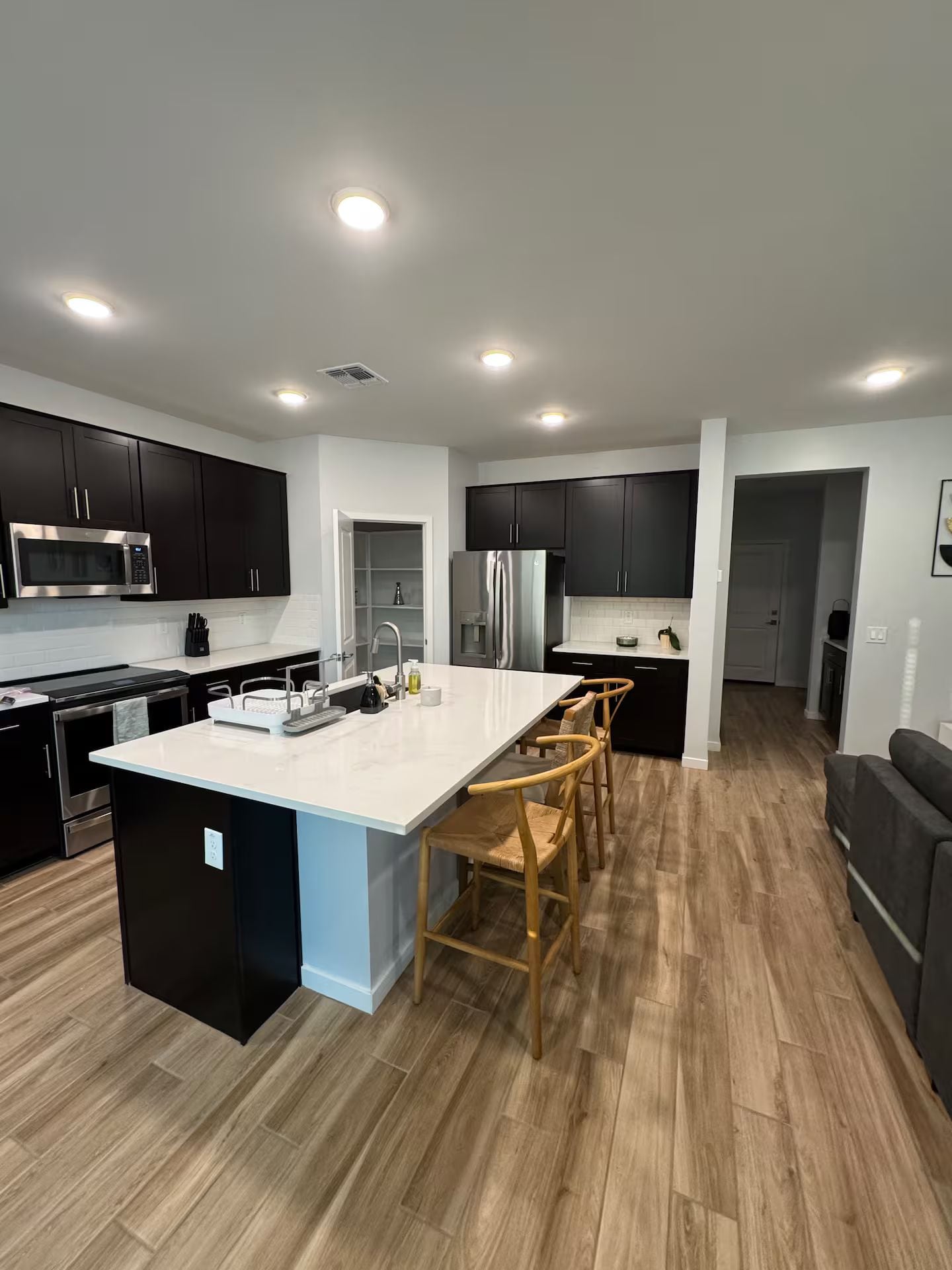 A modern kitchen with dark cabinets, a large island, and a dining area with wooden chairs.
