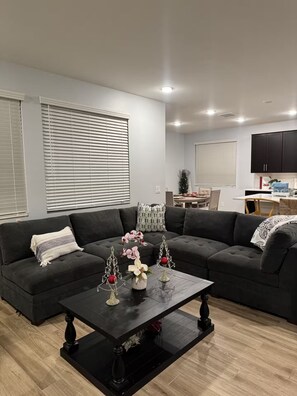 En moderne stue med en hjørnesofa, et sofabord og et spiseområde i baggrunden.