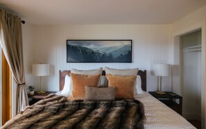 Ein Schlafzimmer mit einem Bett, zwei Nachttischen, einem Wandbild und einem Fellüberwurf.