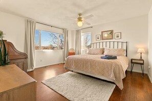 Ein Schlafzimmer mit Bett, Schreibtisch, Stuhl, Stehlampe und Deckenventilator.