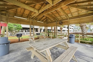 A covered picnic area with wooden benches and picnic tables, a barbecue grill, and trash bins. - Regency Isle 903 (Orange Beach)