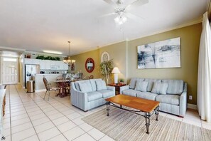A living room with a sofa, coffee table, and a dining area with chairs and a table. - Regency Isle 903 (Orange Beach)