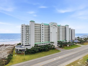 A multi-story hotel with a central courtyard, located near a beach and a road. - Regency Isle 903 (Orange Beach)