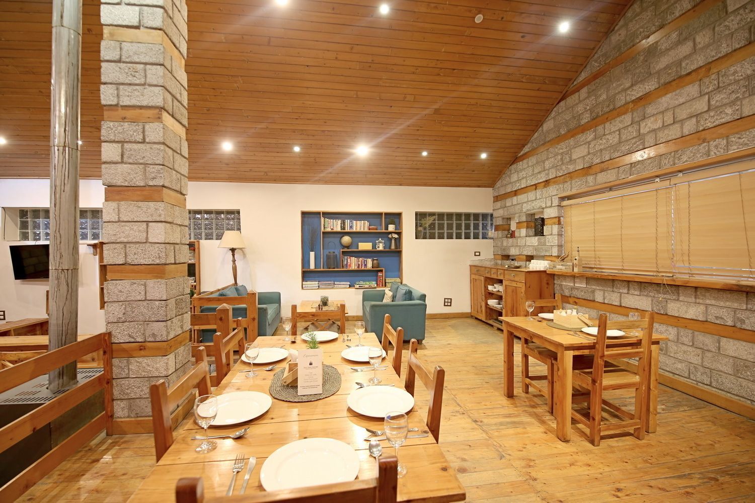 A dining area with wooden tables and chairs, a kitchen area with stone walls, and a seating area with sofas and a coffee table.