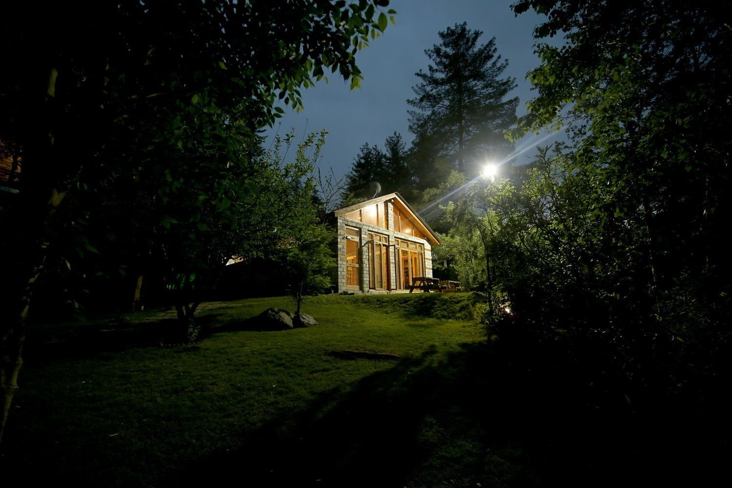 A wooden cabin with a large window, surrounded by trees and a grassy area.