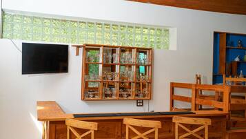 Een kamer met een houten tafel, stoelen, een aan de muur bevestigde televisie en een presentatie van glazen.
