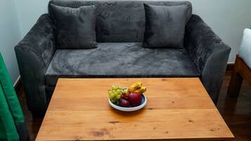 Un sofá gris con una mesa de centro de madera, que presenta un cuenco con fruta.