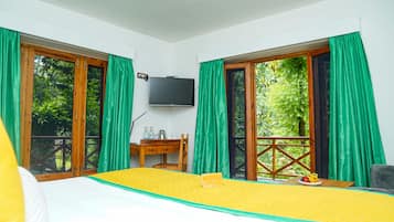 A room with a bed, a desk, a television, and large windows with curtains.