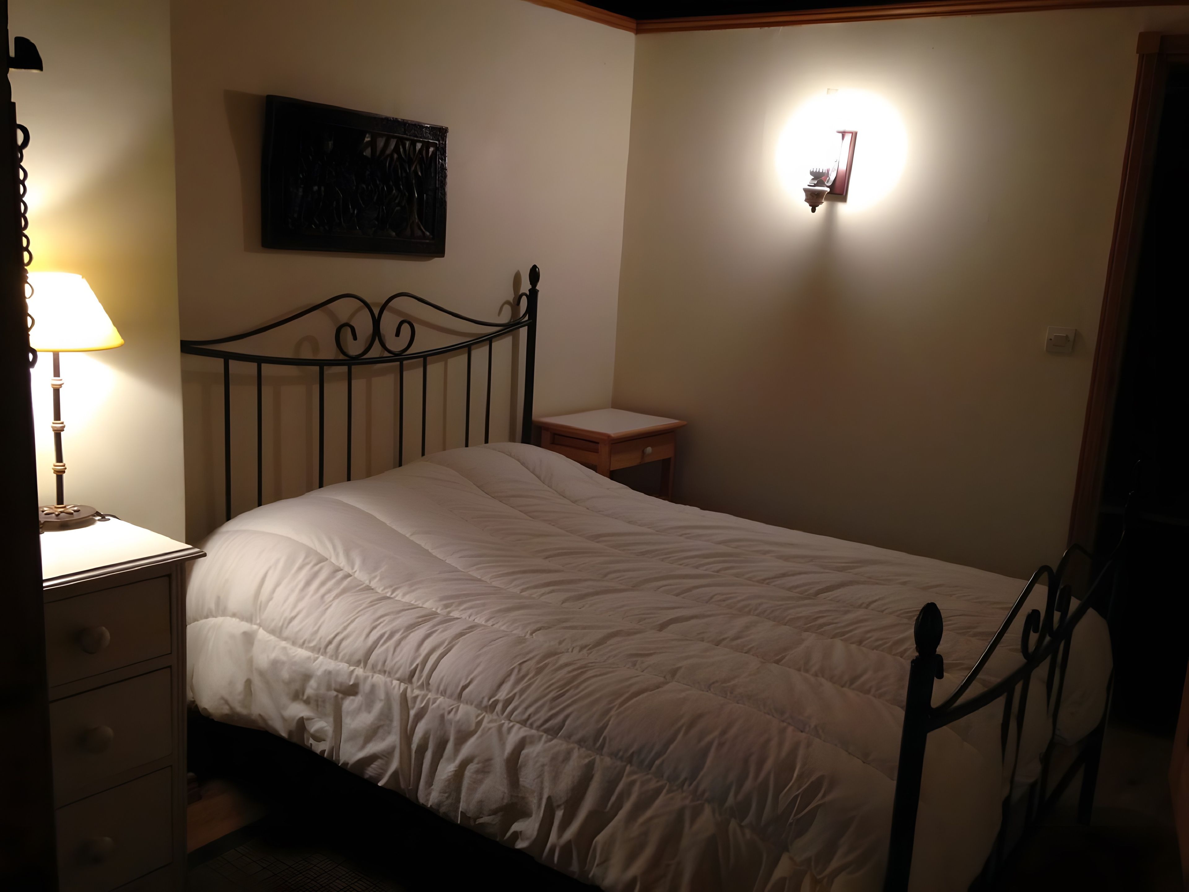 A bedroom with a single bed, a nightstand, a wall-mounted light, and a small table.