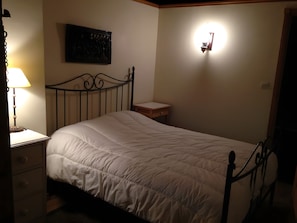 A bedroom with a single bed, a nightstand, a wall-mounted light, and a small table. - Holiday Home 'L'ecurie' with Mountain View (Vira)