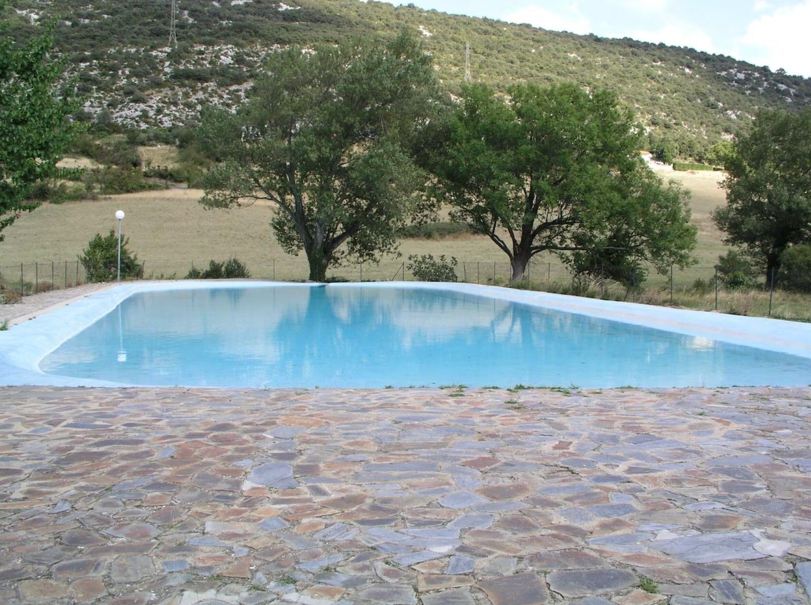 Una piscina con bordo in pietra circondata da alberi e un paesaggio collinare.
