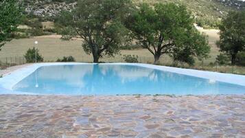 Una piscina con bordo in pietra circondata da alberi e un paesaggio collinare.